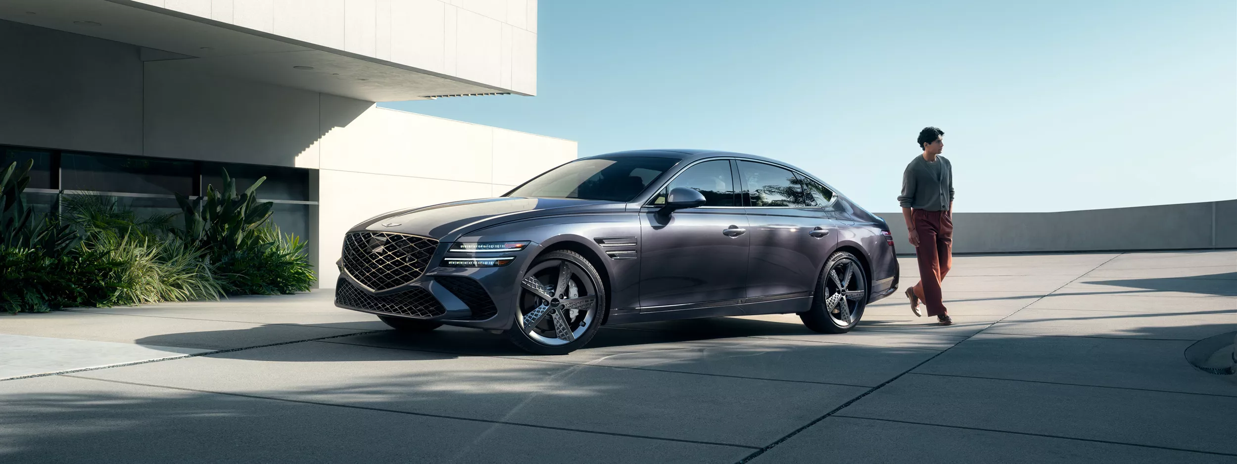 7/8 front driver side view of Genesis G80 in Ceres Blue parked next to modern house with man nearby