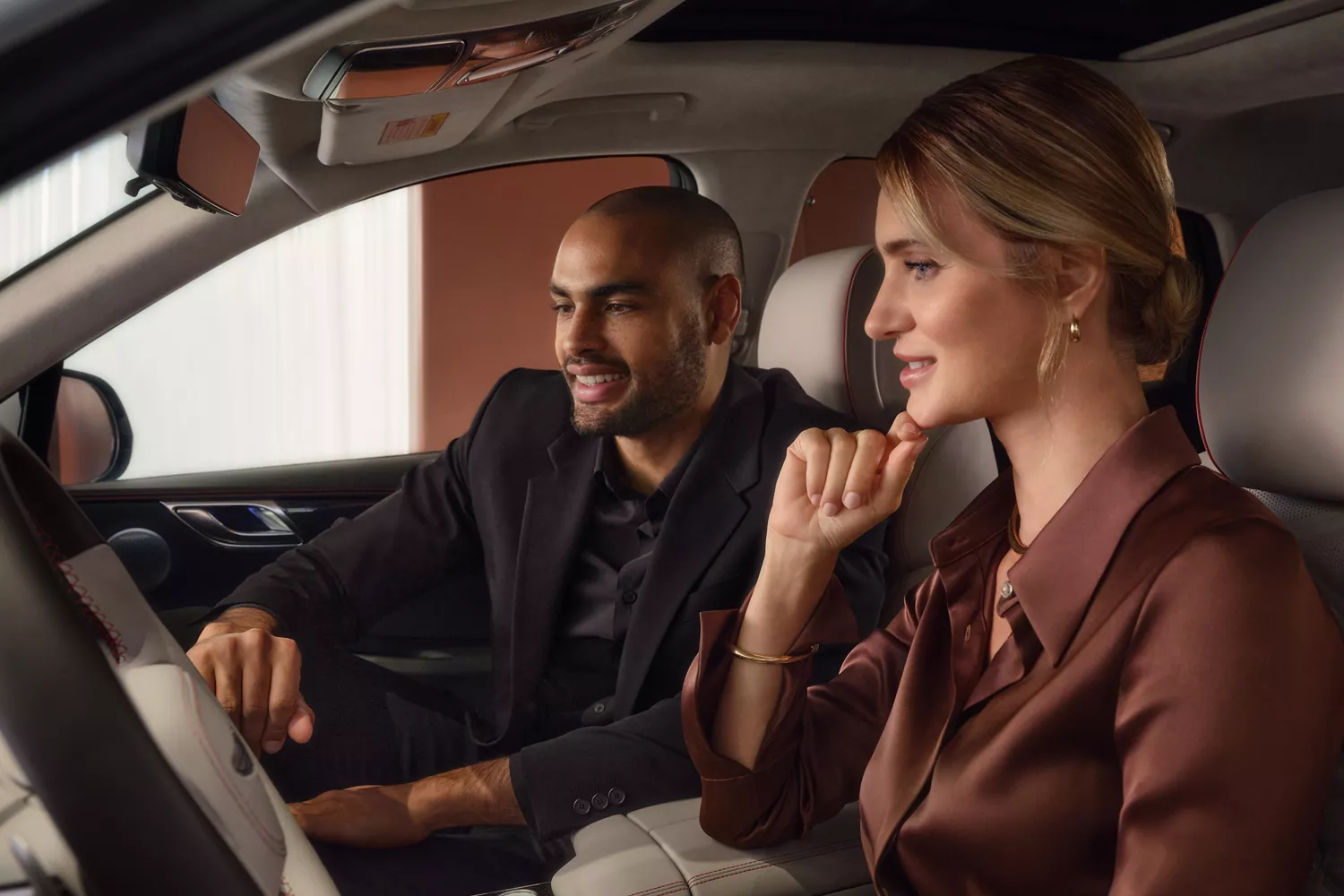 Interior view of a luxury genesis vehicle with two passengers exploring dashboard features