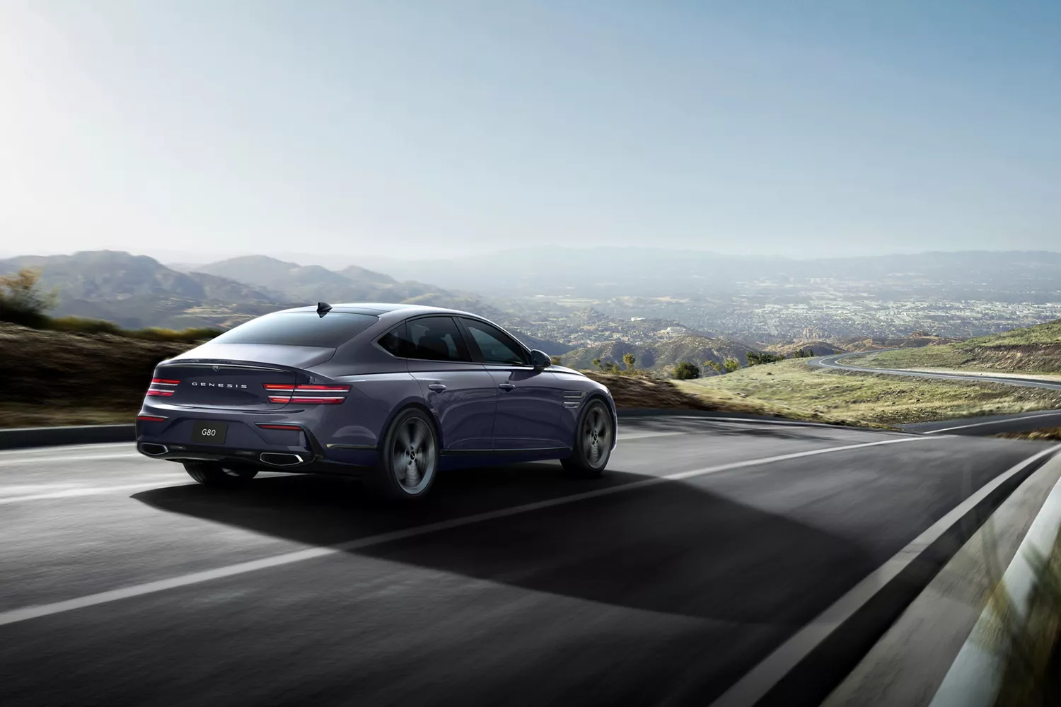 3/4 rear passenger side view of Genesis G80 Ceres Blue, in motion driving on road with rolling hills